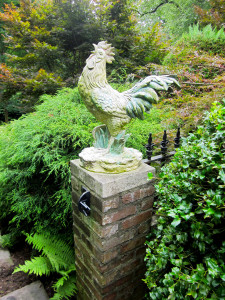 A rooster sculpture claims center stage, strutting before a beautiful woodland setting.
